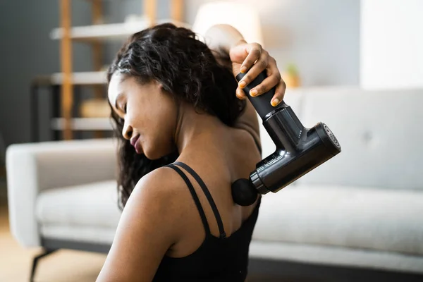 Femme qui utilise un pistolet de massage pour le dos à la maison