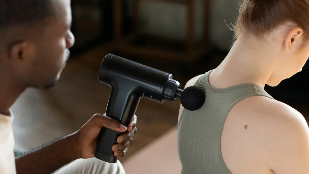 Homme utilisant un pistolet de massage débutant pour détendre le dos d’une femme