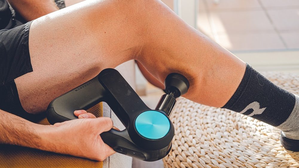 Personne utilisant un pistolet de massage articulations sur un muscle de la jambe après le sport